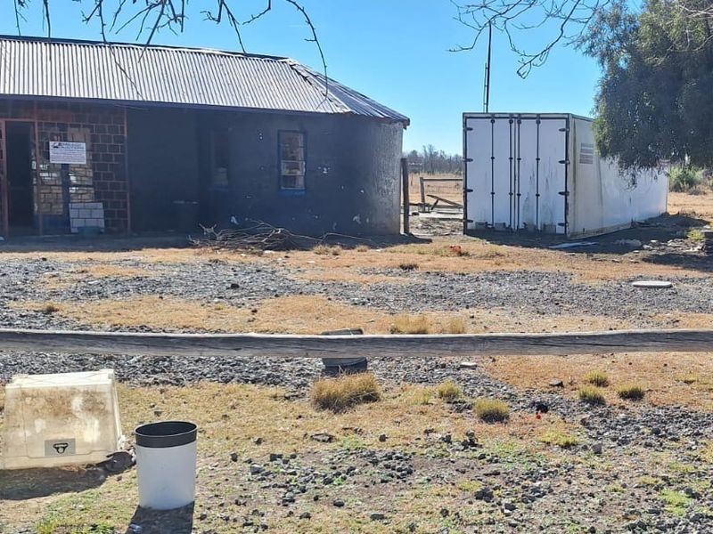 Exterior view of a small holding property featuring a brick structure with a corrugated iron roof and an adjacent shipping container unit.