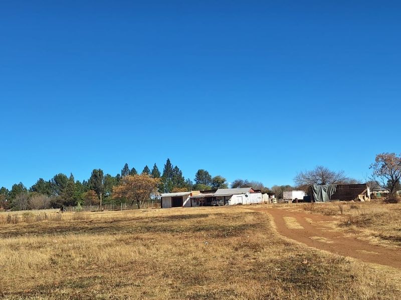 A wide-angle view of a small holding property featuring a dirt driveway leading toward the main dwelling and various outbuildings on a large plot.