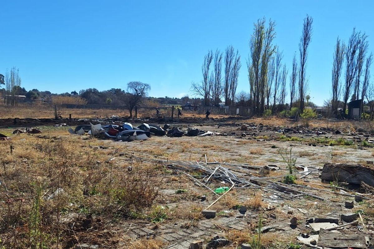 An expansive, undeveloped outdoor area featuring a paved section, currently covered in debris and overgrown vegetation, requiring significant clearing and landscaping.