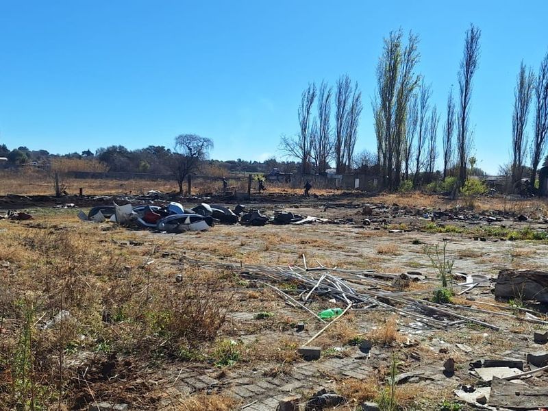 An expansive, undeveloped outdoor area featuring a paved section, currently covered in debris and overgrown vegetation, requiring significant clearing and landscaping.