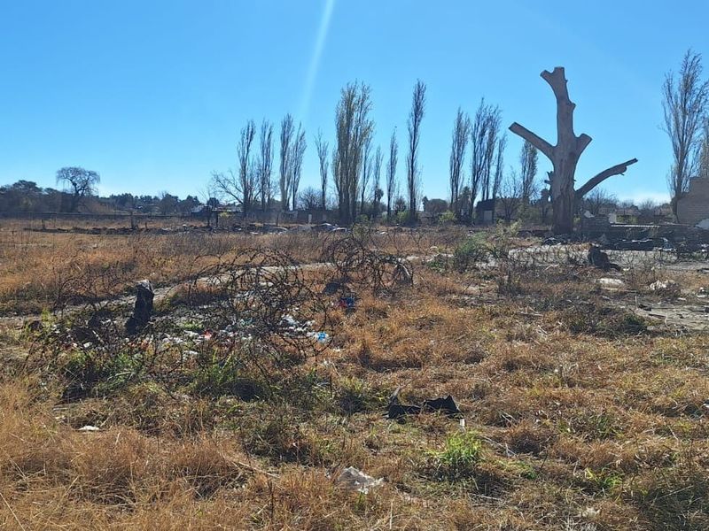 An expansive, undeveloped plot of land featuring dry vegetation, scattered debris, and remnants of barbed wire fencing.