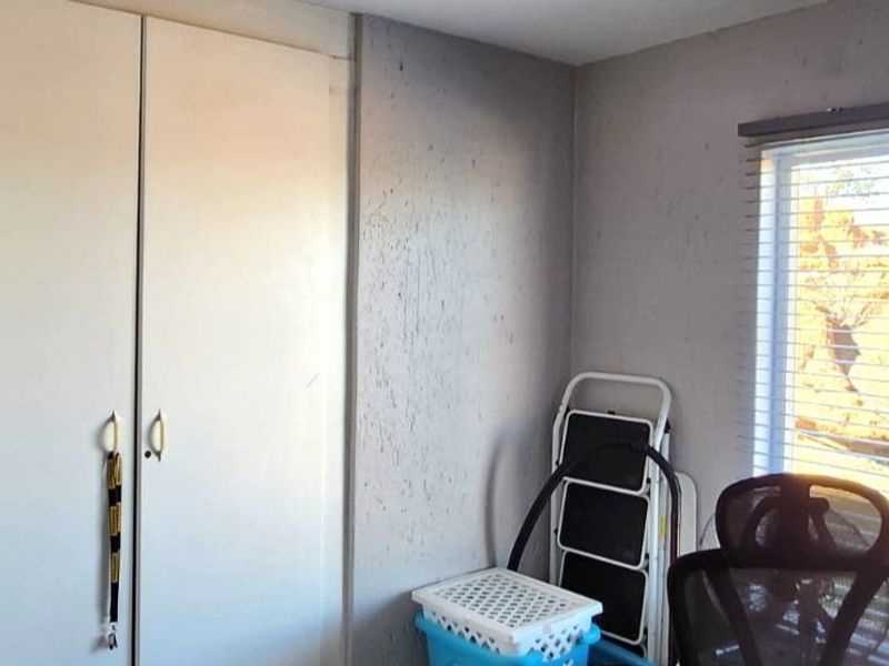 A bedroom featuring built-in cupboards and venetian blinds, requiring cosmetic updates to the wall finishes to improve the overall aesthetic.