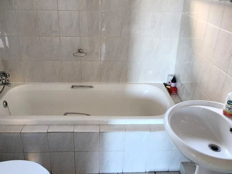 A functional bathroom featuring a standard bathtub, pedestal basin, and tiled walls, offering a clean and practical space.