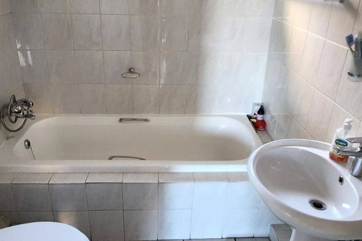 A functional bathroom featuring a standard bathtub, pedestal basin, and tiled walls, offering a clean and practical space.
