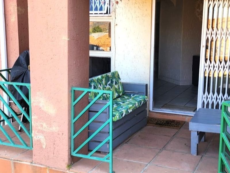 A covered patio area featuring tiled flooring, metal security gates, and structural columns, providing an outdoor transition space to the interior of the townhouse.