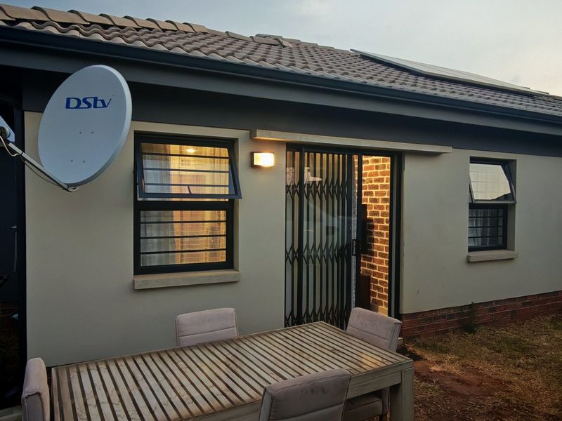 Rear exterior view of the property featuring a tiled roof, solar panels, security gate, and satellite dish installation.