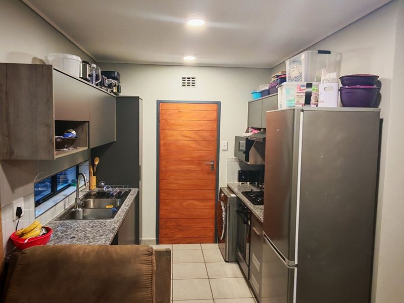 A functional kitchen featuring granite countertops, built-in cabinetry, a stainless steel double sink, and integrated cooking appliances with tiled flooring.