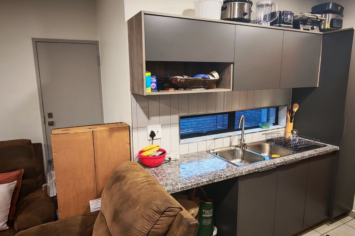 Compact kitchen area featuring modern grey cabinetry, granite countertops, a stainless steel double sink, and a tiled splashback with a horizontal window.