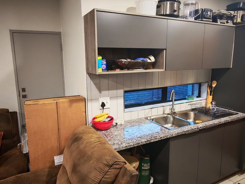 Compact kitchen area featuring modern grey cabinetry, granite countertops, a stainless steel double sink, and a tiled splashback with a horizontal window.