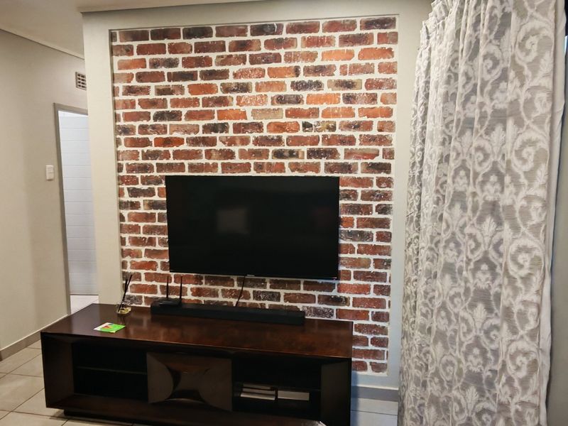 Living area featuring a prominent exposed brick feature wall and neutral tiled flooring.