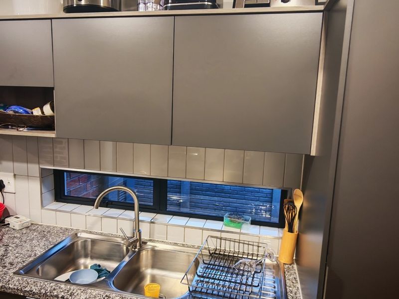 A modern kitchen area featuring dark grey cabinetry, a granite countertop, a double stainless steel sink with a gooseneck faucet, and a subway tile backsplash.