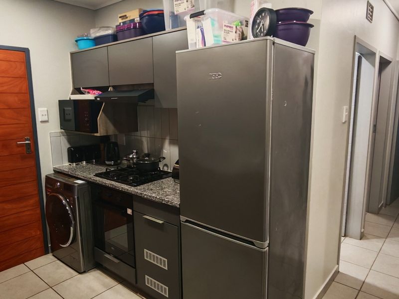 Compact kitchen featuring grey cabinetry, granite countertops, built-in oven, gas hob, and tiled flooring, with direct access to the hallway.