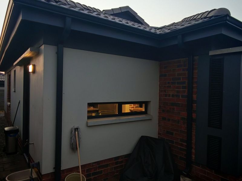 A view of the rear exterior of the house featuring a combination of brick and plastered walls, tiled roofing, and functional guttering.