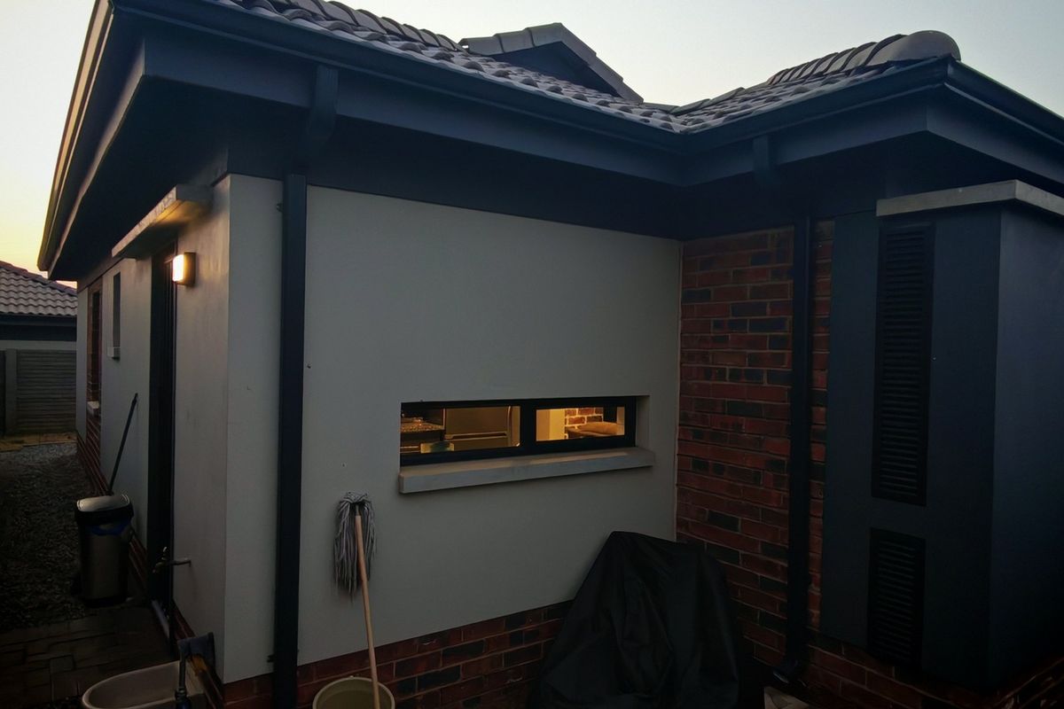 A view of the rear exterior of the house featuring a combination of brick and plastered walls, tiled roofing, and functional guttering.