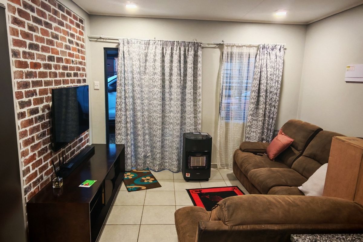 A living room featuring an exposed brick accent wall, tiled flooring, and direct access to the exterior via a sliding door.