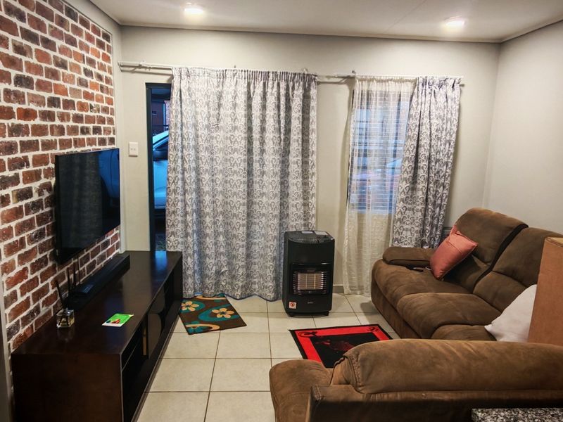 A living room featuring an exposed brick accent wall, tiled flooring, and direct access to the exterior via a sliding door.