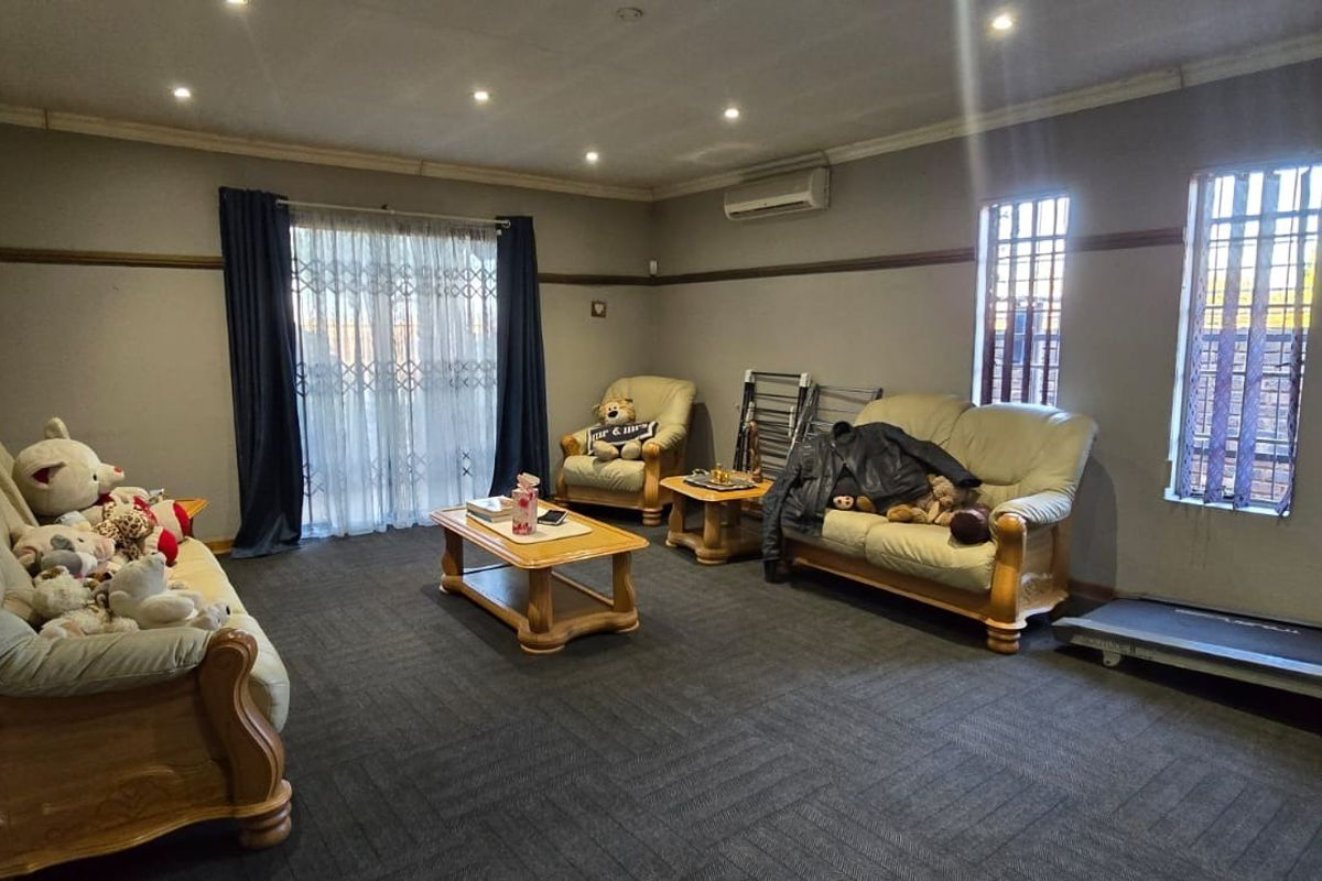 A spacious living room featuring carpet flooring, recessed downlighting, a wall-mounted air conditioner, and security bars on the windows.