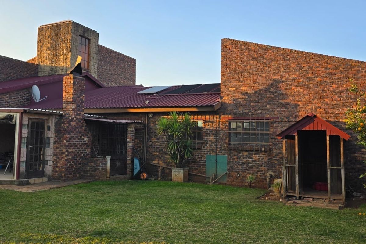 Rear view of a face brick house featuring a covered patio, corrugated metal roof with solar panels, and a well-maintained garden area.