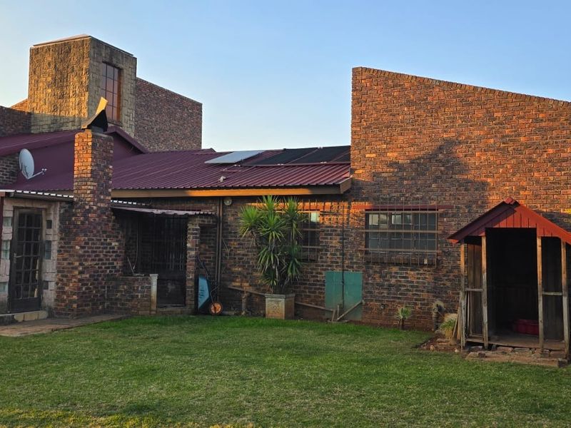 Rear view of a face brick house featuring a covered patio, corrugated metal roof with solar panels, and a well-maintained garden area.