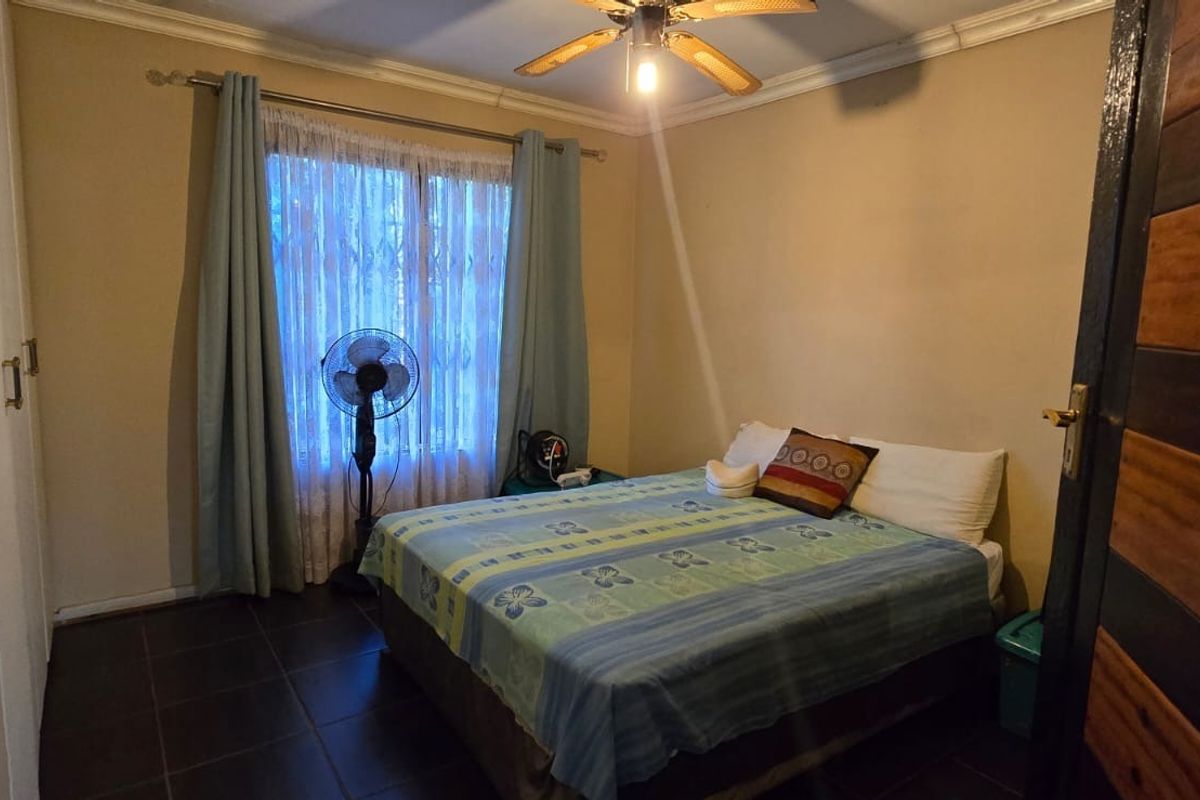 A functional bedroom featuring tiled flooring, built-in cupboards, and a ceiling fan, with a window secured by a metal gate.