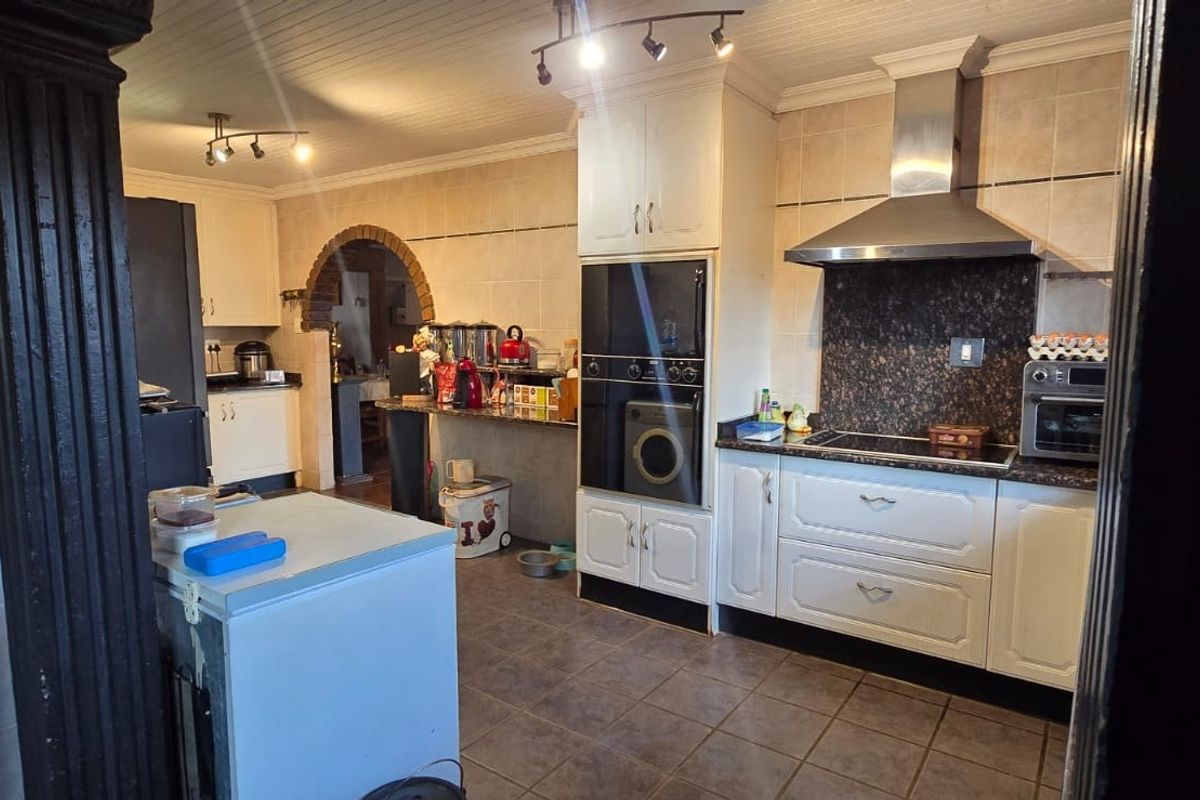 A functional kitchen featuring built-in cabinetry, granite countertops, a stainless steel extractor fan, and tiled flooring with a beadboard ceiling.