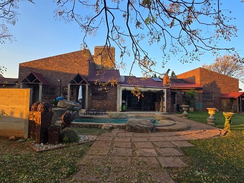 Rear view of the property featuring a brick facade, a swimming pool with rock features, and a paved patio area set within a private garden.