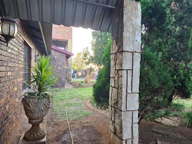 A covered patio area featuring stone-clad pillars and brick walls, overlooking a garden space with mature trees.