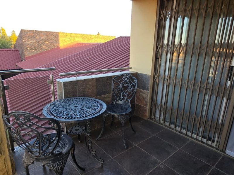A private balcony featuring tiled flooring, stone wall cladding, and a modern stainless steel and glass balustrade overlooking the surrounding roofline.