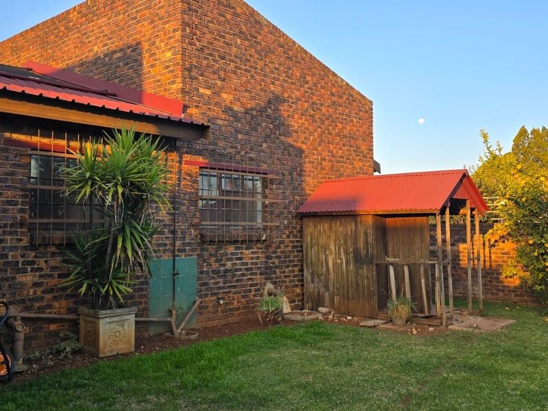 Rear view of the property featuring face brick exterior, corrugated metal roofing, security bars on windows, and a small garden area with a wooden structure.