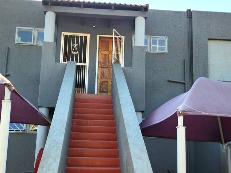 Front exterior view of a townhouse featuring a central staircase leading to the entrance with security gate and timber door.