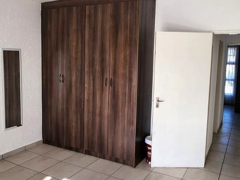 A bedroom featuring built-in wooden cupboards and tiled flooring, leading into a hallway.