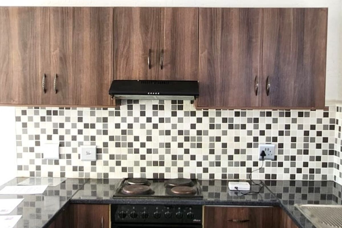 A functional kitchen area featuring dark wood-look cabinetry, a mosaic tile backsplash, granite countertops, and a built-in electric hob with an extractor fan.