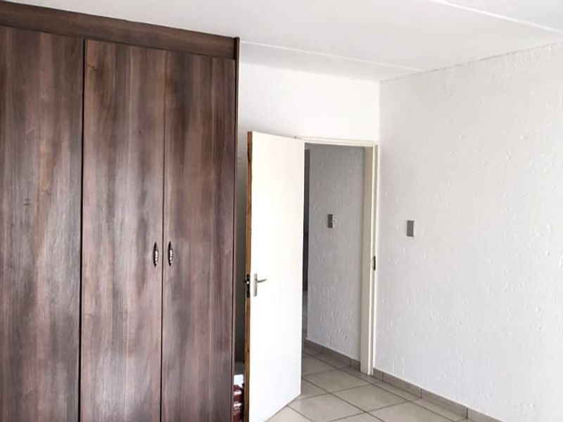 A bedroom featuring built-in wooden cupboards, tiled flooring, and neutral white walls, offering a clean and functional space.