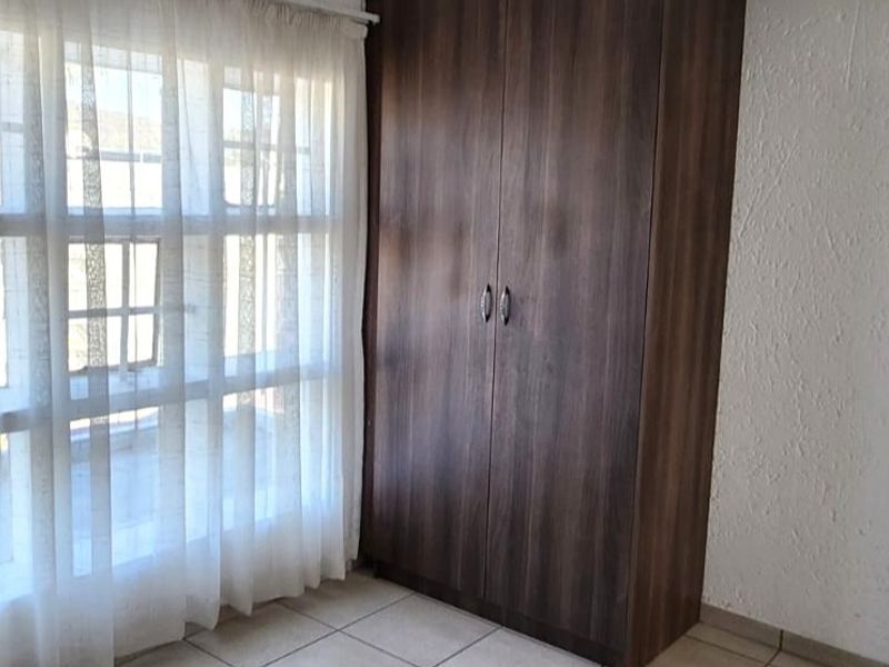A bright bedroom featuring tiled flooring and a dark wood built-in wardrobe, offering a clean and functional space.