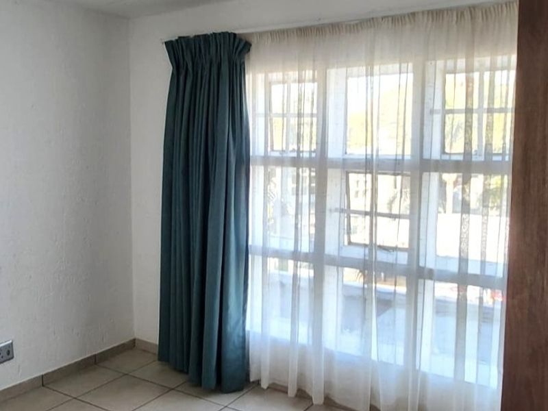 An empty bedroom featuring tiled flooring and a large multi-pane window with curtains, requiring minor cosmetic updates to the wall finishes.