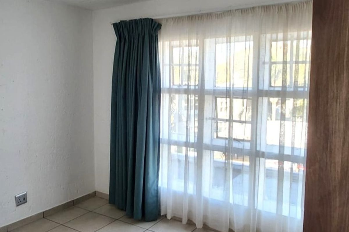 An empty bedroom featuring tiled flooring and a large multi-pane window with curtains, requiring minor cosmetic updates to the wall finishes.
