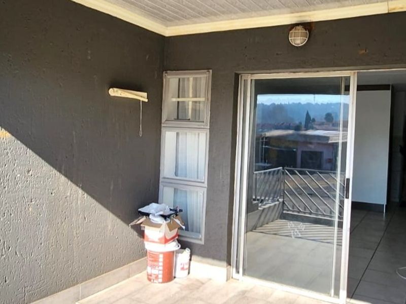 A covered balcony area featuring tiled flooring, a sliding glass door entrance, and exterior wall lighting, offering a functional outdoor space.