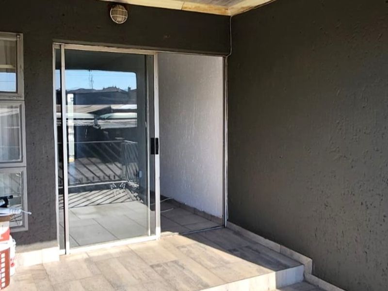 A covered patio area featuring tiled flooring, a sliding glass door entrance, and exterior wall lighting, providing a functional outdoor transition space.