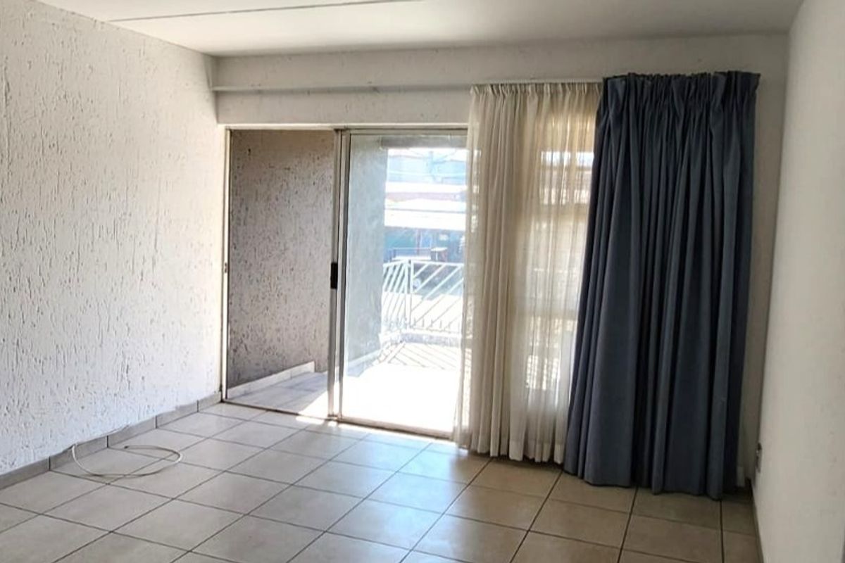 An empty living room featuring tiled flooring, textured walls, and a sliding glass door providing access to an outdoor patio area.