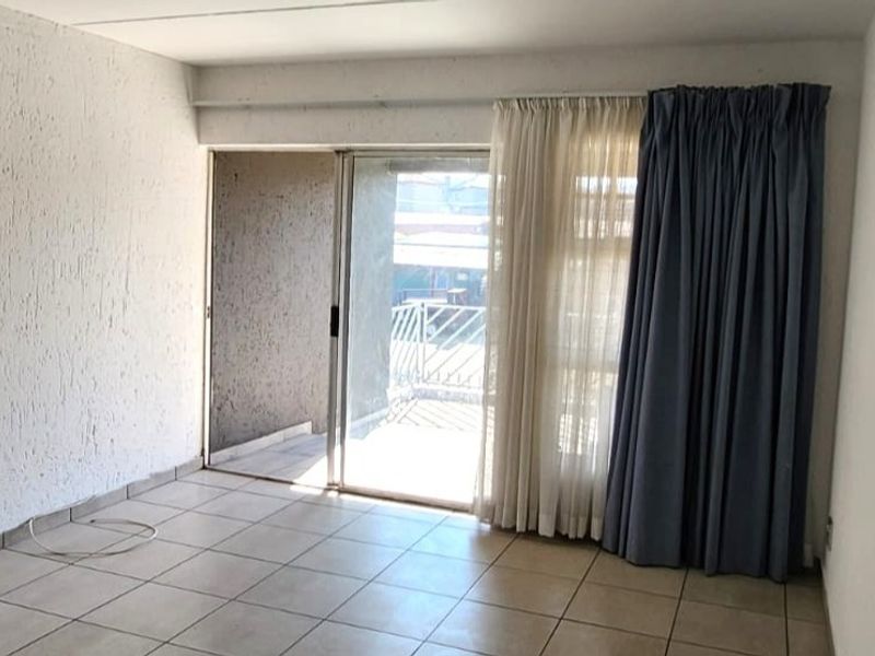An empty living room featuring tiled flooring, textured walls, and a sliding glass door providing access to an outdoor patio area.