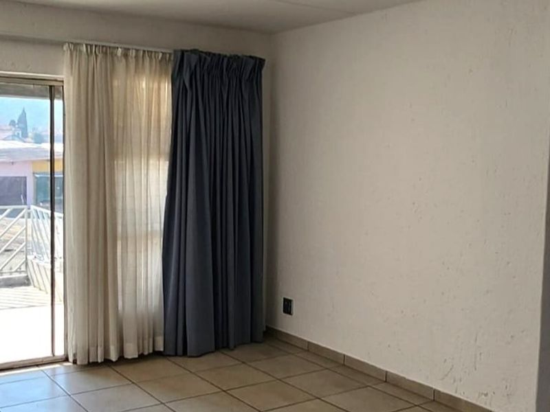 An empty living room featuring ceramic floor tiles, textured walls, and a sliding glass door leading to an outdoor balcony area.