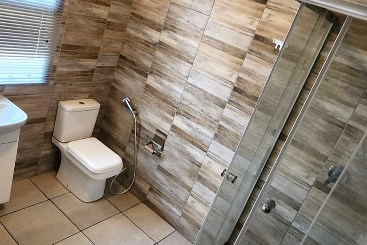 A modern bathroom featuring wood-look wall tiles, a glass shower enclosure, a vanity unit with a basin, and a toilet with a bidet spray.