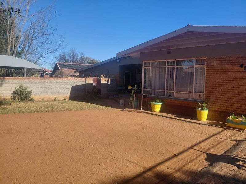 Front view of a brick house featuring a large window with security bars, a perimeter wall, and an unpaved yard area.