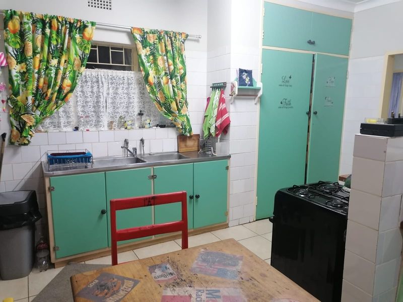 A functional kitchen featuring a double basin stainless steel sink, tiled splashback, and ample built-in cabinetry with a dedicated pantry cupboard.