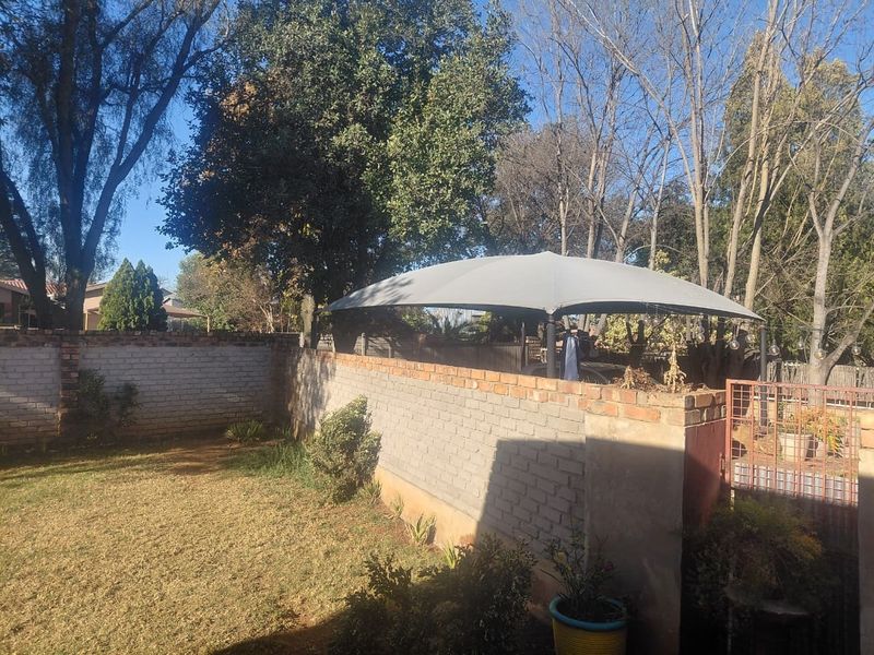 A private garden area featuring a brick boundary wall, a shade sail structure, and a metal gate entrance.