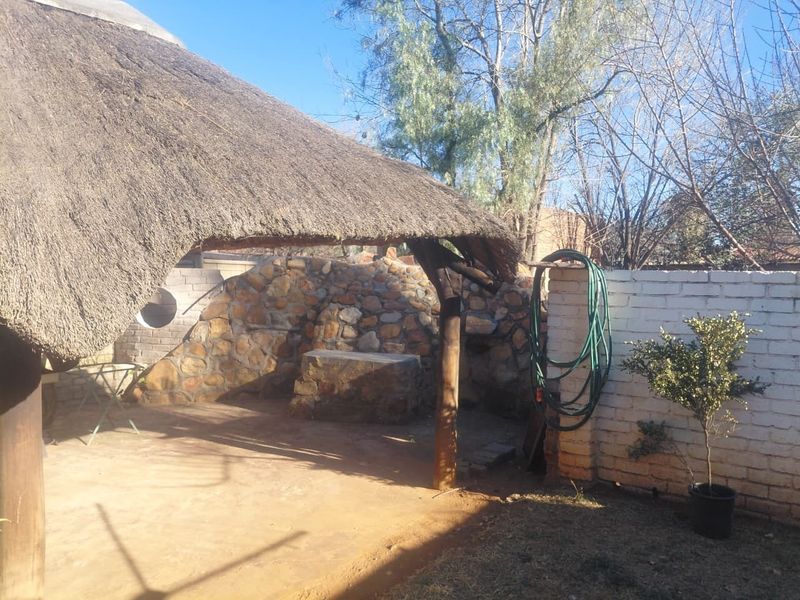 Outdoor entertainment area featuring a traditional thatch roof, built-in stone braai, and rustic stone cladding, offering a potential space for garden relaxation.