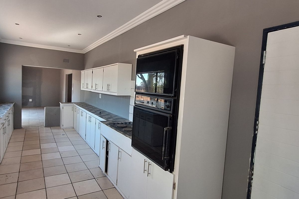 A spacious, empty kitchen featuring white cabinetry, built-in oven and microwave, tiled flooring, and neutral grey walls, offering a clean canvas for updates.