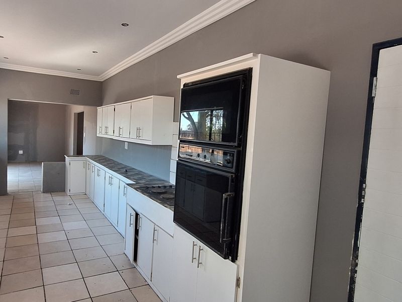 A spacious, empty kitchen featuring white cabinetry, built-in oven and microwave, tiled flooring, and neutral grey walls, offering a clean canvas for updates.