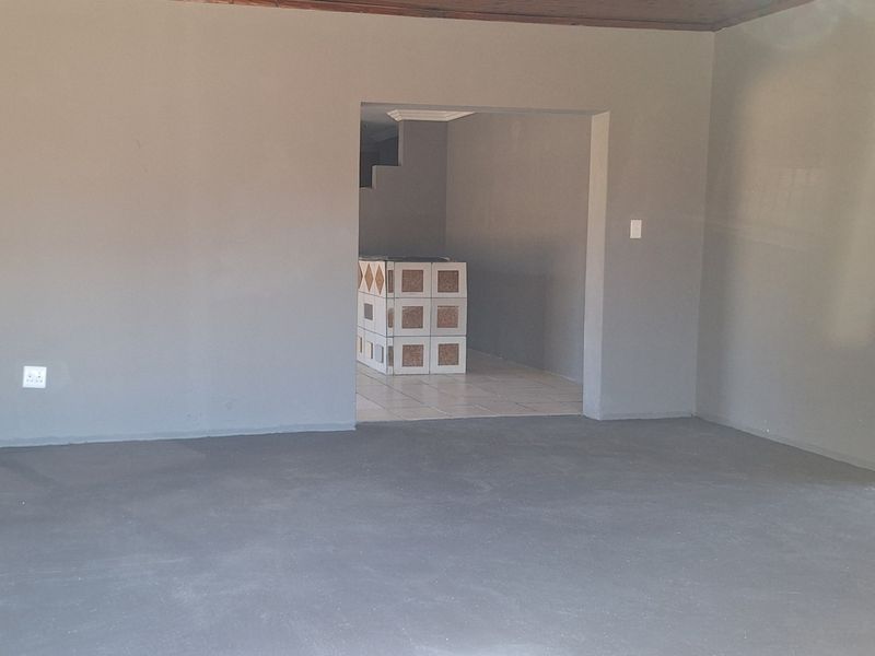 An empty, unfinished living area featuring exposed concrete flooring and a timber ceiling, providing a blank canvas for renovation and interior design.