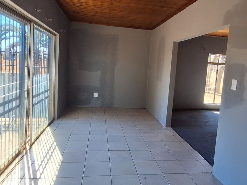 An empty living area featuring tiled floors, a timber ceiling, and large sliding glass doors with security gates, currently undergoing wall painting.
